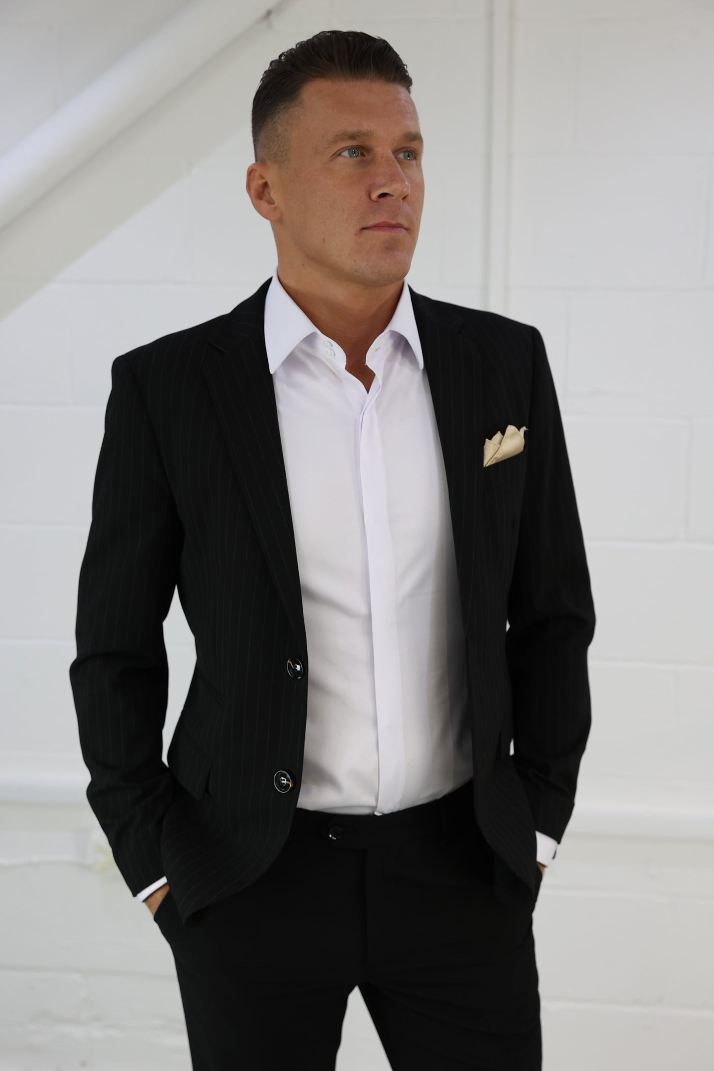Man wearing a black pinstripe blazer paired with a crisp white shirt and gold pocket square; a versatile and stylish option from Suitbae, available individually in skinny fit, slim fit, tailored fit, big & tall, XL, and larger men's sizes, suitable for both formal and smart-casual occasions.