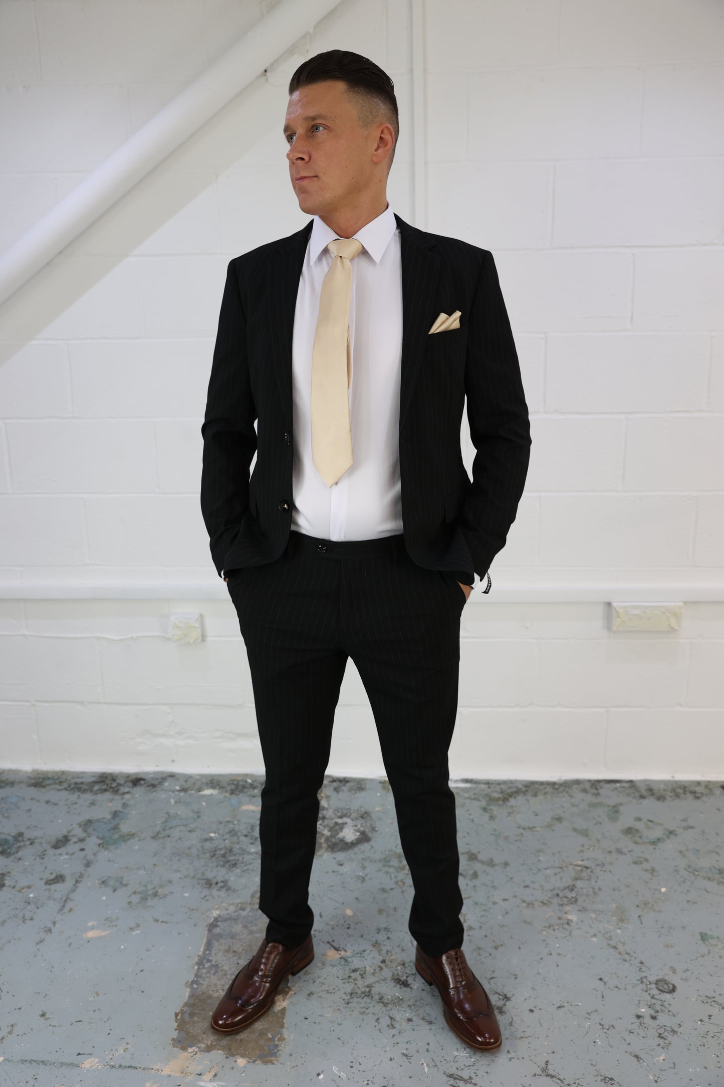 Man wearing a Suitbae black pinstripe two-piece suit, featuring a tailored blazer and slim-fit trousers, paired with a crisp white shirt, gold tie, and pocket square; perfect for formal and smart-casual occasions.