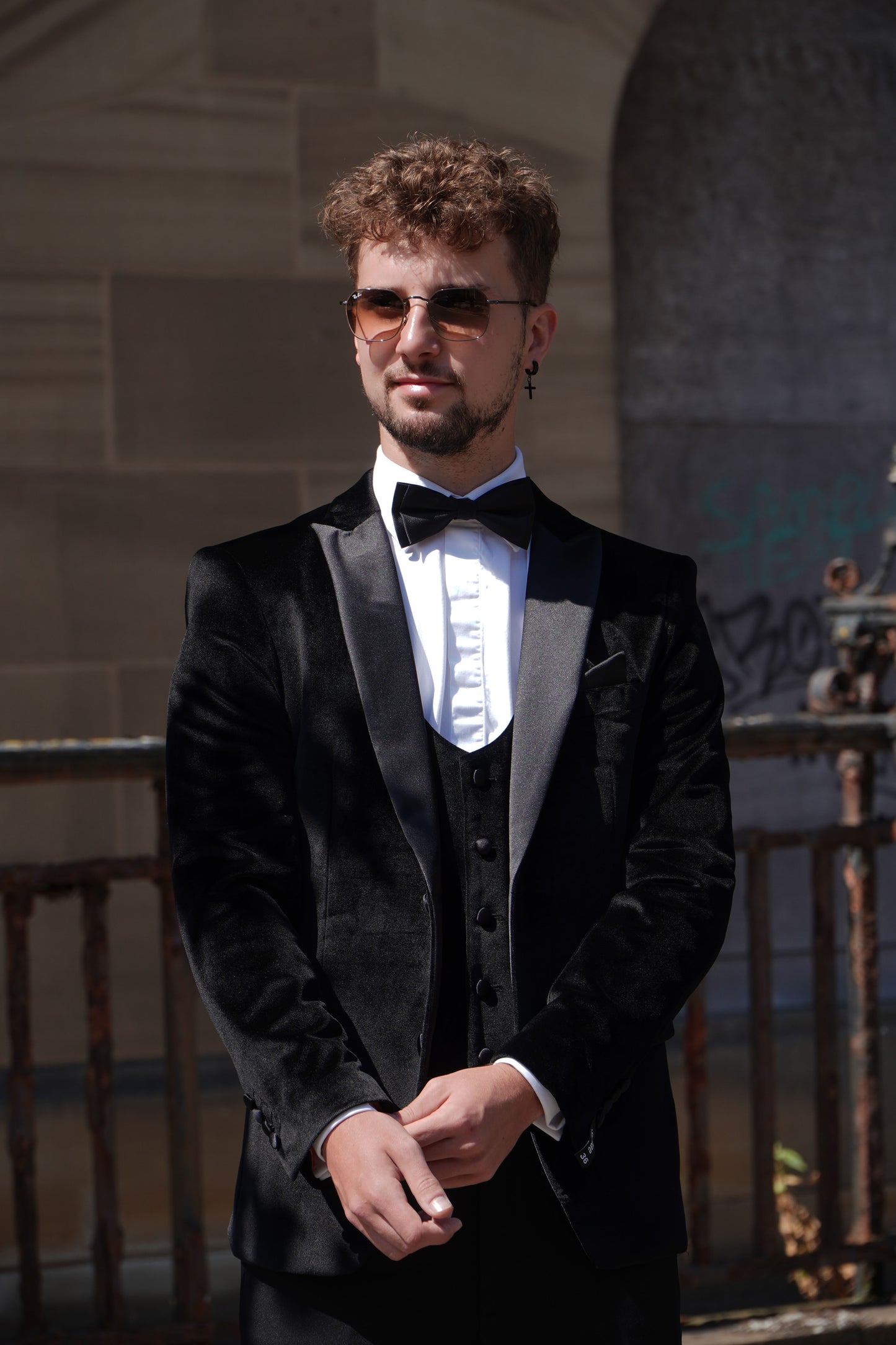 Model wearing the SUITBAE Black Velvet Three-Piece Tuxedo — featuring a satin peak lapel velvet blazer, matching waistcoat and trousers, styled with a bow tie for weddings and black-tie events.