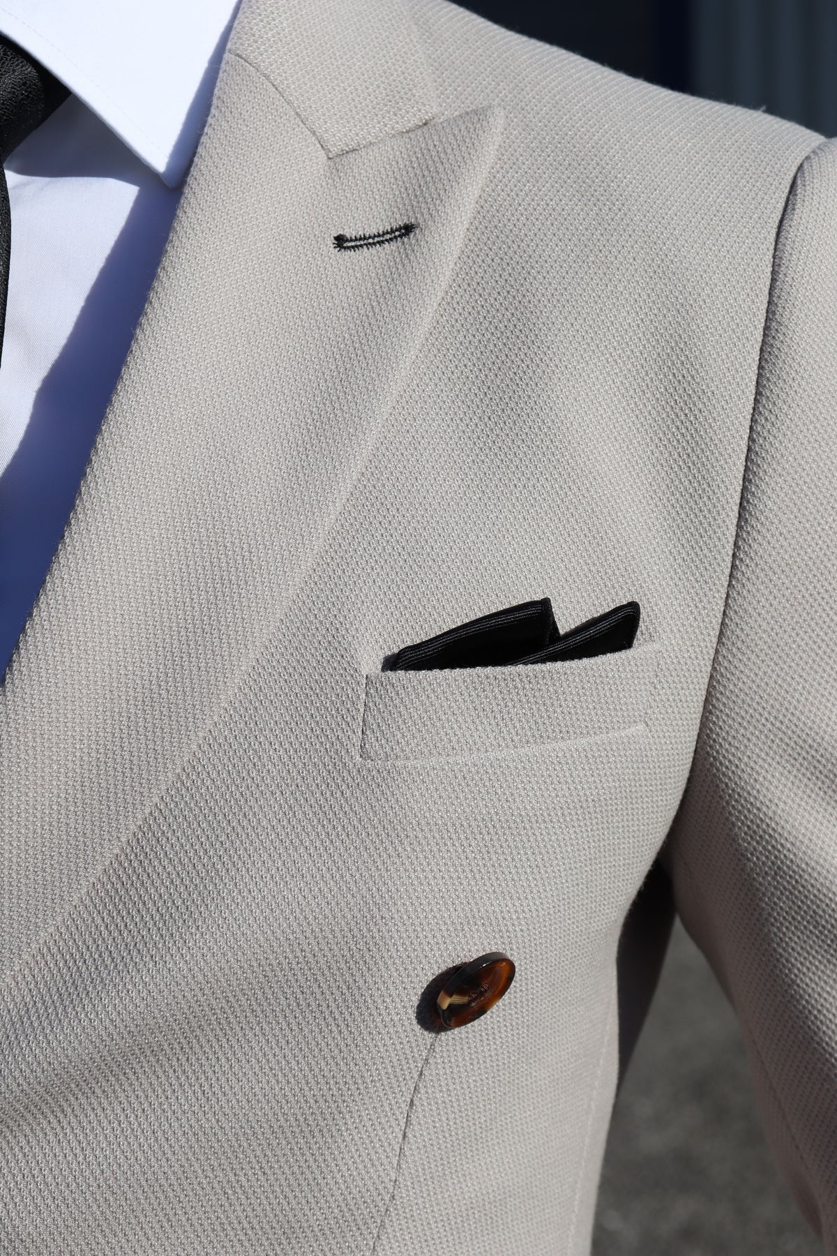 Close-up of the SUITBAE Escobar Stone Double-Breasted Contrast Suit showing textured stone fabric, dark tortoiseshell buttons, and a black pocket square — tailored perfection for weddings and formal events.