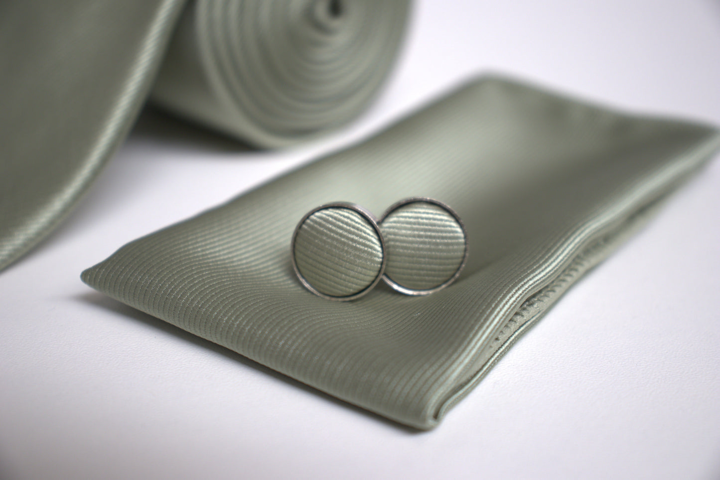 Close-up of sage green pocket square and cufflinks, elegant groomsmen accessories for prom, races and special occasions.