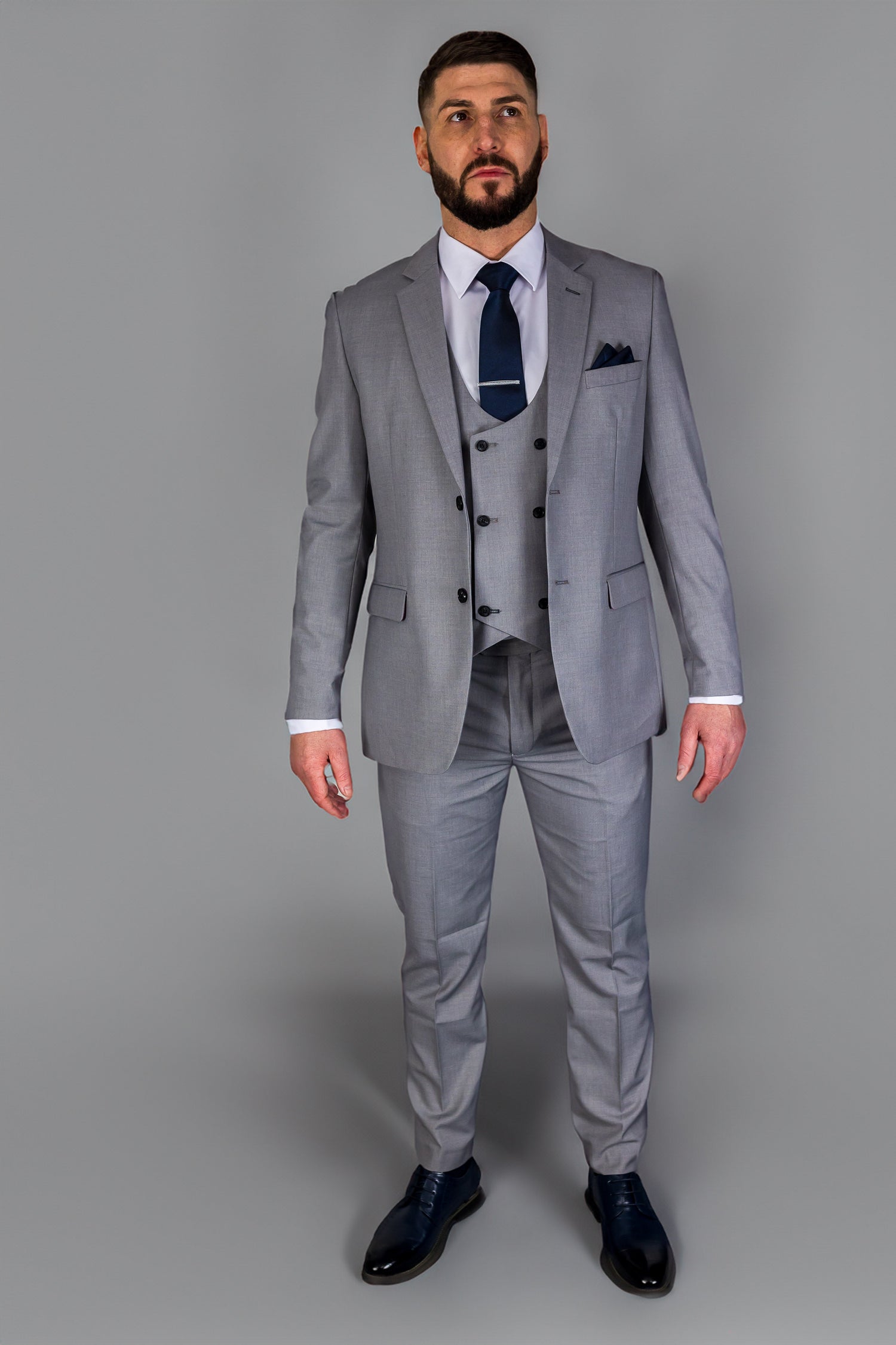 Man wearing a sharp grey three-piece suit with a navy tie, ideal for weddings, business meetings, and formal events.