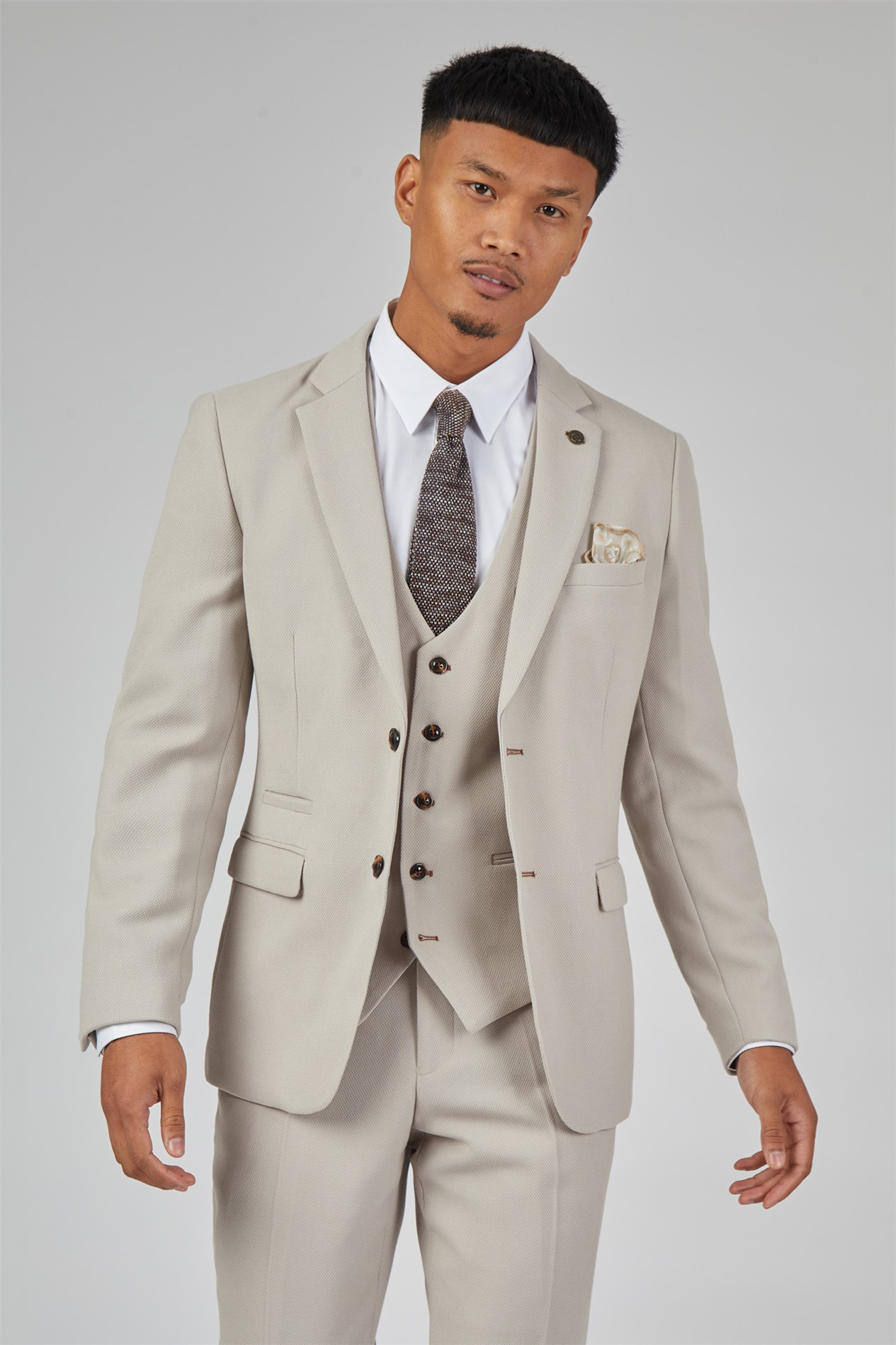 Man wearing a Marc Darcy HM5 beige three-piece suit with matching vest, white shirt, patterned tie, and beige pocket square. This stylish suit offers a modern, tailored fit, perfect for weddings, business, and formal occasions.