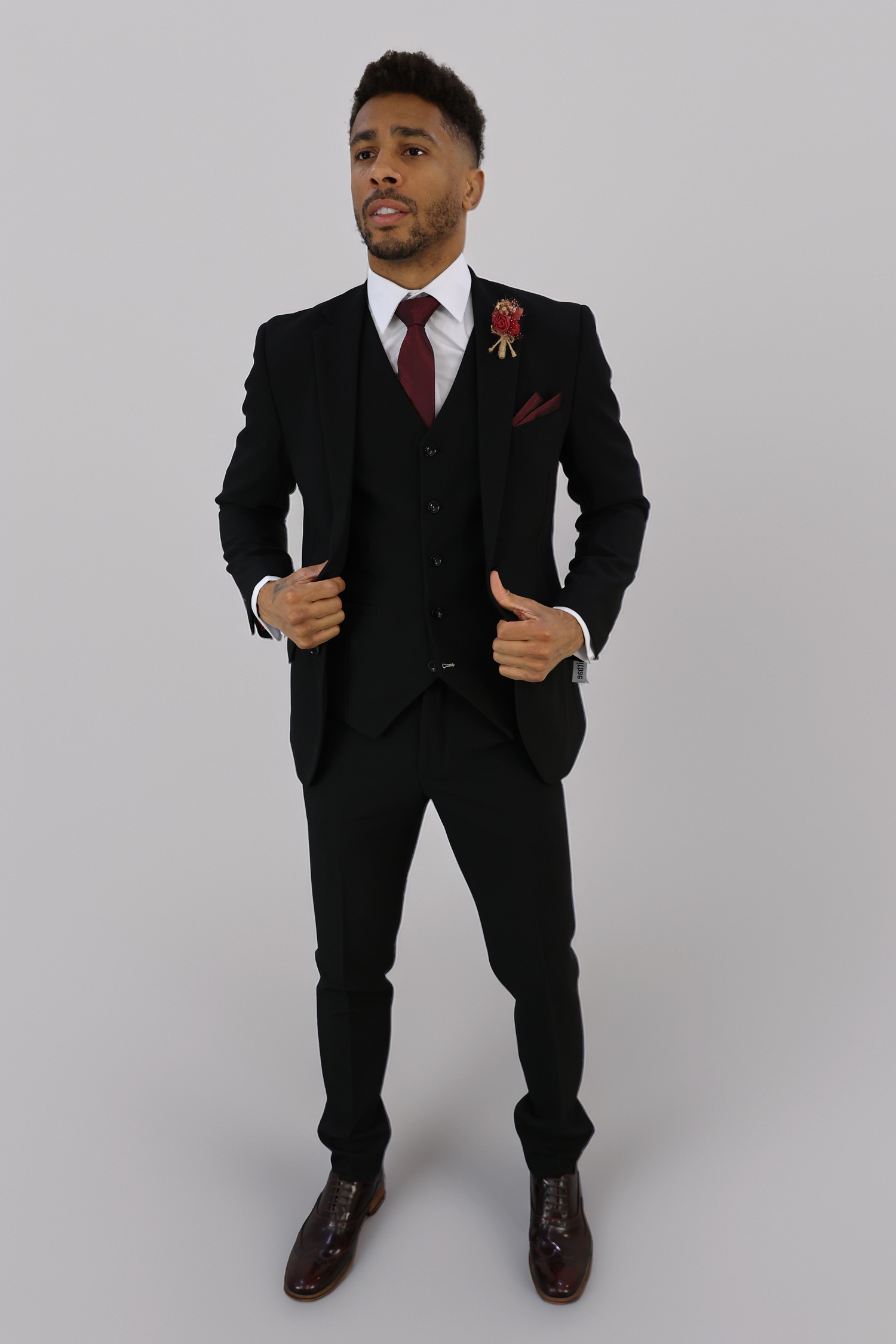 Close-up of a black tailored suit with satin lapels, paired with a red paisley tie and matching pocket square. The elegant formalwear is perfect for weddings, business events, and special occasions, offering a classic and sophisticated look.