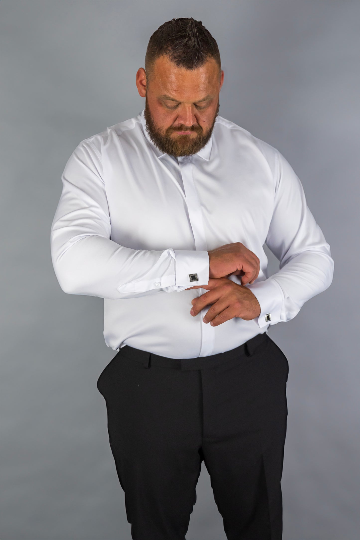 Man wearing a white dress shirt with cufflinks and black trousers, adjusting his sleeve. The formal shirt features a classic fit, perfect for business, weddings, and special occasions, providing a sharp, sophisticated look.