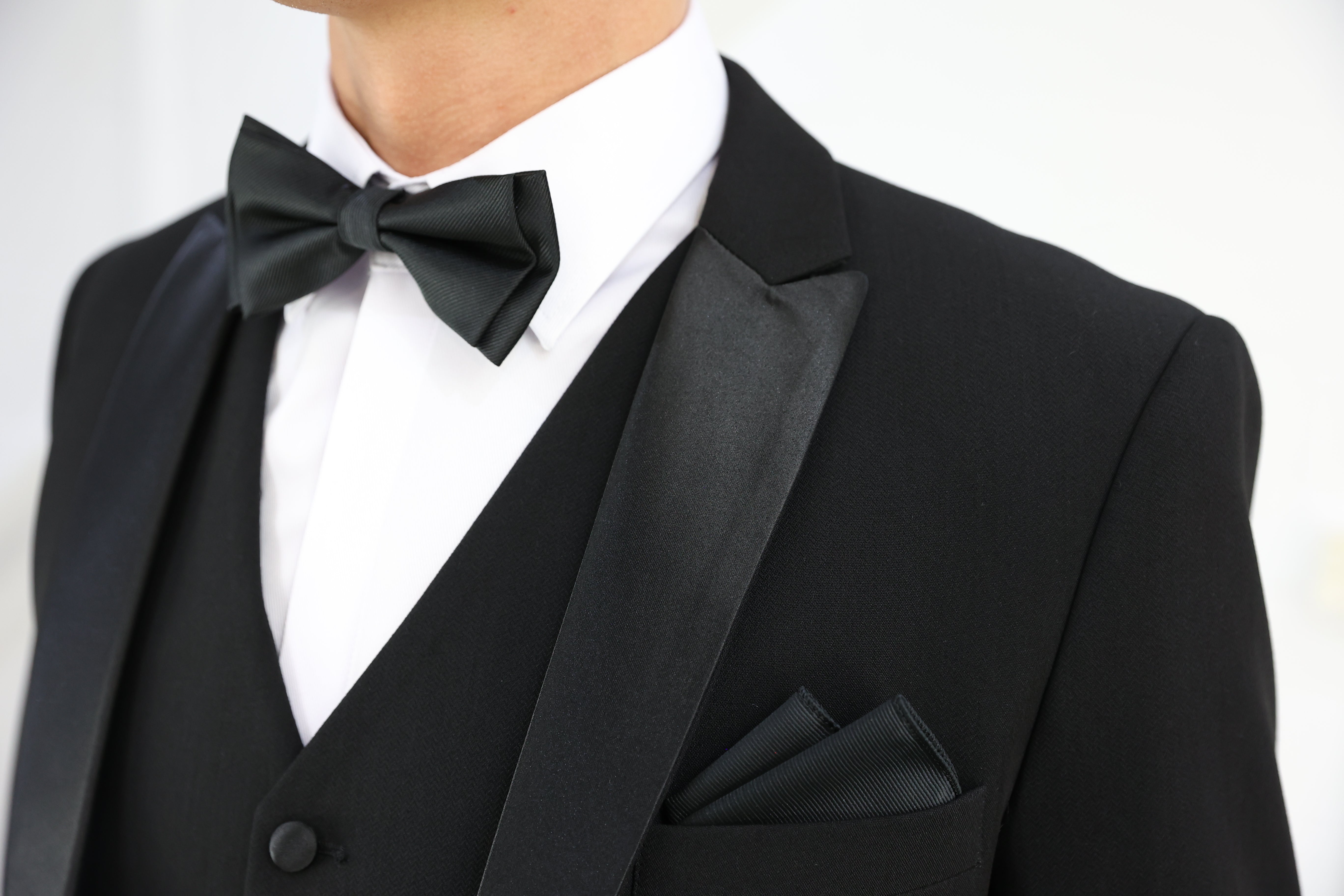 Close-up of the SUITBAE Diablo Black Three Piece Tuxedo, featuring a satin peak lapel, matching black bow tie, and folded pocket square — classic black-tie style for formal events, proms, or weddings.