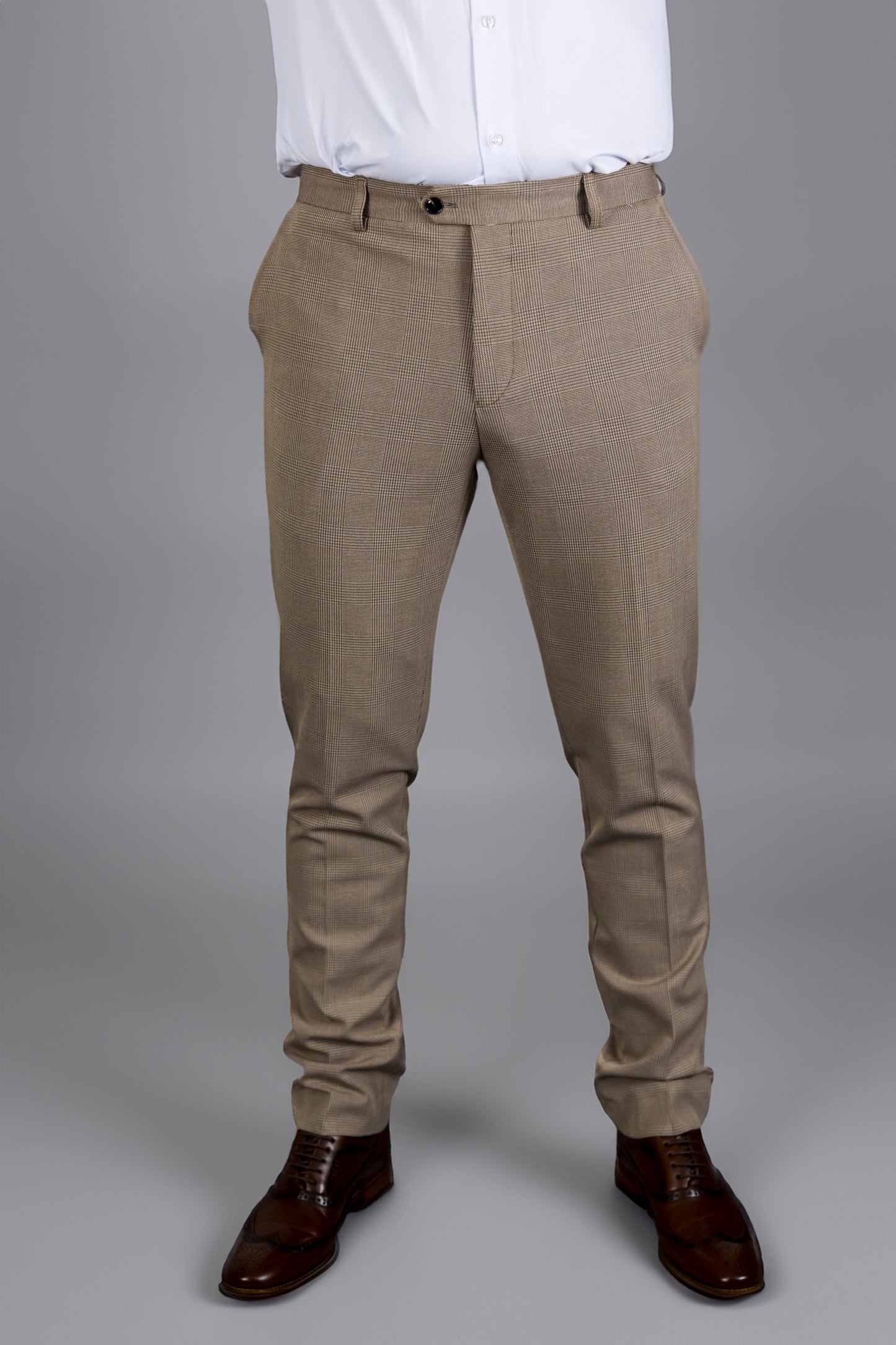 A close-up of the Suitbae Charles beige suit trousers, featuring a Prince of Wales check pattern. These slim fit trousers have a tailored cut, belt loops, and front pockets, offering a modern and polished look. Paired with brown brogue shoes, they are ideal for formal occasions, business meetings, or weddings. The beige colour and subtle pattern provide a refined touch to classic menswear.