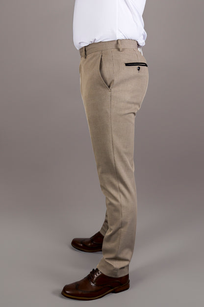 A side view of the Suitbae Charles beige suit trousers, featuring a Prince of Wales check pattern. The slim fit design has front and back pockets with contrasting black piping on the back, enhancing the tailored look. Paired with brown brogue shoes, the trousers provide a refined silhouette, ideal for formal wear, business meetings, or special occasions. The beige colour and subtle pattern add sophistication to the classic menswear style.