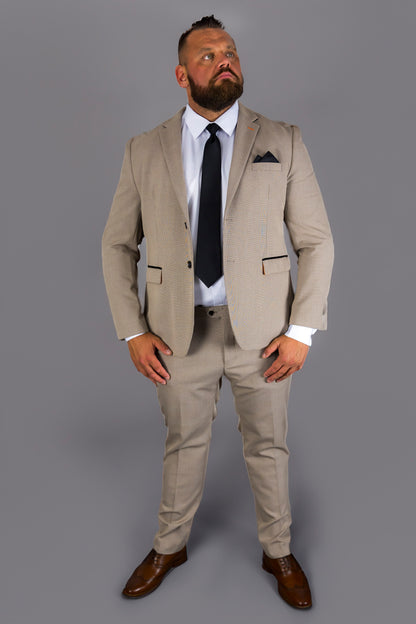 A man models the Suitbae Charles beige suit in a big and tall plus size fit. The suit features a Prince of Wales check pattern, styled with a white shirt, black tie, and dark pocket square. The tailored jacket and slim fit trousers provide a polished look, paired with brown shoes. Designed for a refined appearance for larger frames.