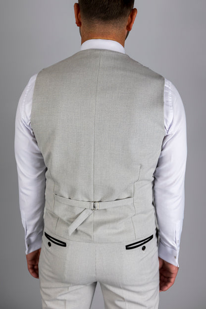 Back view of a model wearing the Suitbae Charles stone waistcoat with adjustable back strap for a tailored fit. The waistcoat features a subtle Prince of Wales check pattern, paired with matching trousers that have black contrast piped pockets, highlighting modern British tailoring.