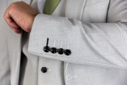 Close-up of the Suitbae Charles stone suit sleeve showing a four-button cuff detail with contrast stitching. The suit features a subtle Prince of Wales check pattern in a light stone colour, providing a refined and elegant look. Ideal for formal occasions, highlighting intricate tailoring details.