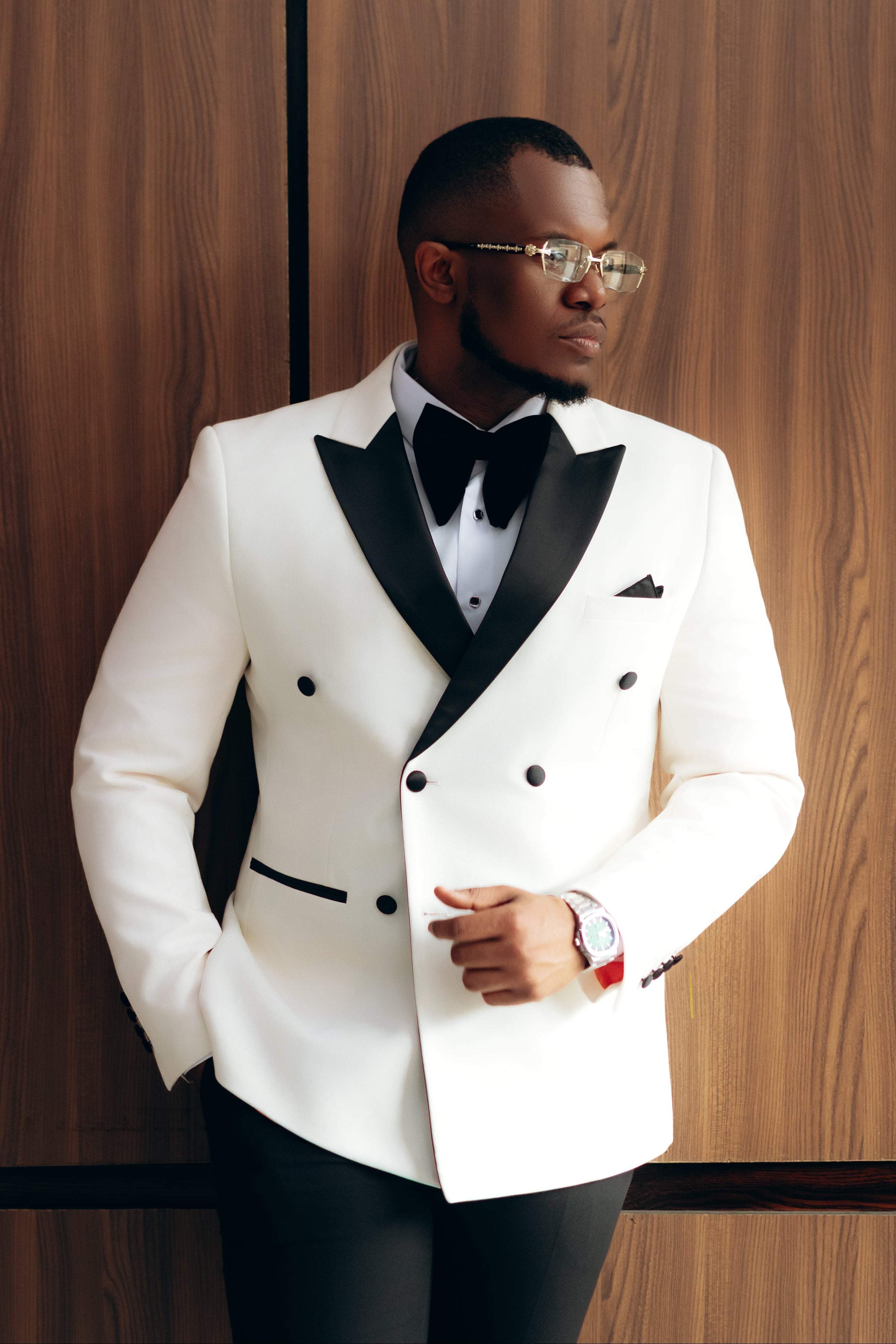 Man wearing a white double-breasted tuxedo jacket with black satin lapels, black bow tie and black trousers at a formal event.