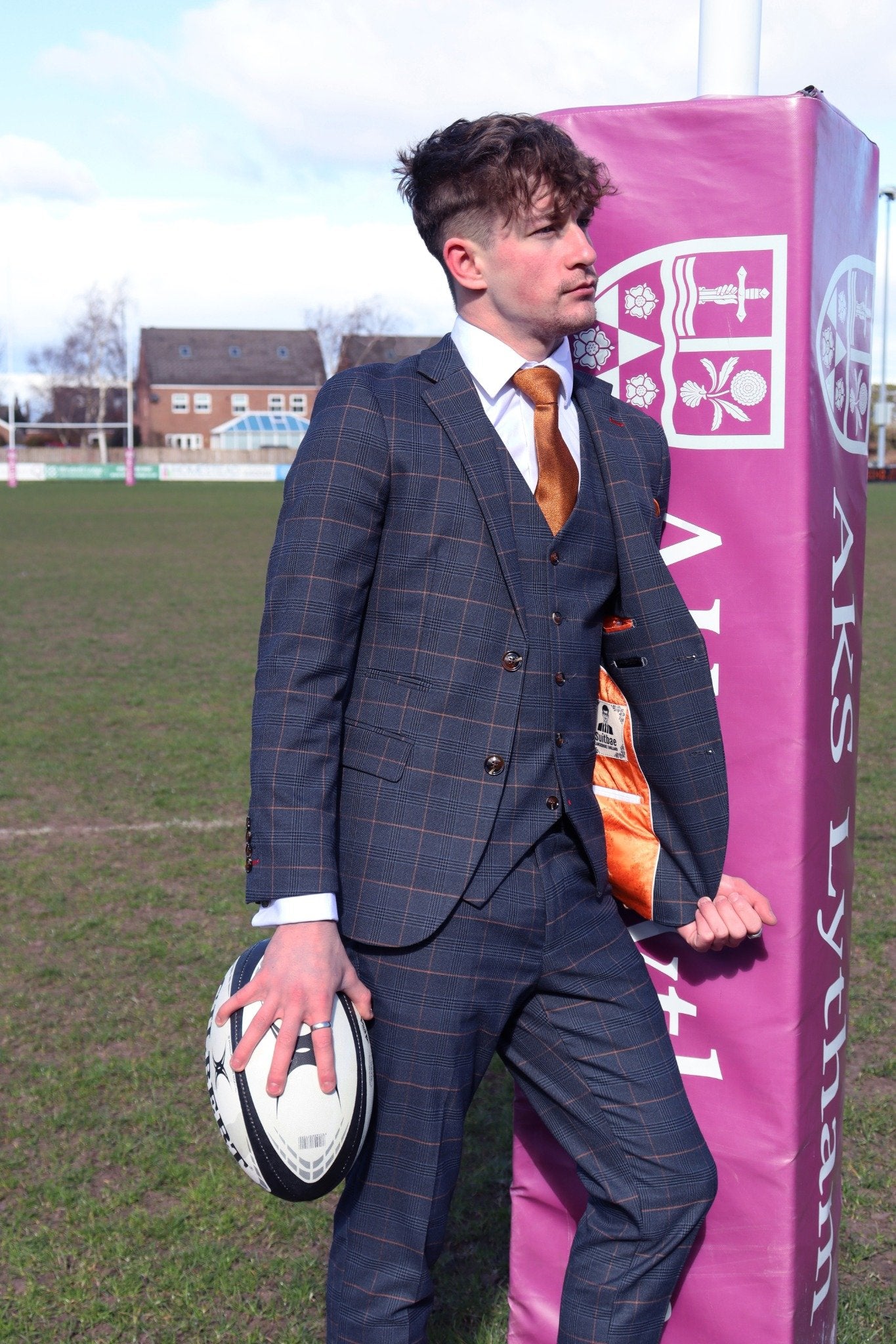 Model wearing the SUITBAE Thomas Navy Check Three-Piece Suit — navy blue design with burnt orange check pattern, styled with a copper tie and orange lining, ideal for weddings, race days and formal occasions.