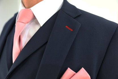 Close-up of a navy suit jacket lapel with red buttonhole stitching, paired with a pink tie and pocket square, showcasing Suitbae's attention to detail and expert craftsmanship. Perfect for XL, Plus Size, and Big & Tall men's sizes. Available at Suitbae.com