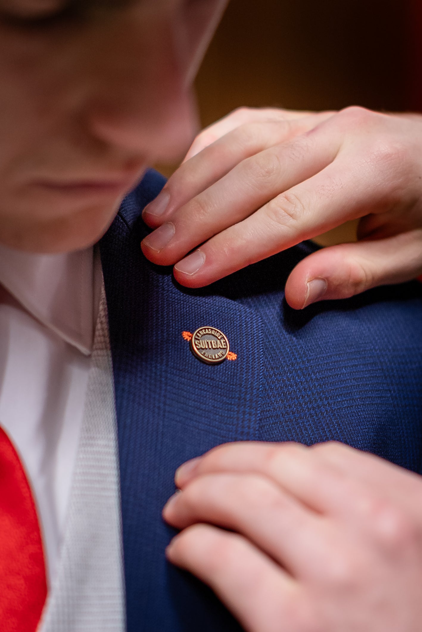 Close-up of a Barnsley FC player wearing the SUITBAE Charles Navy Contrast Three-Piece Suit, featuring a red tie, light waistcoat, and a gold SUITBAE lapel pin being adjusted on the jacket collar.