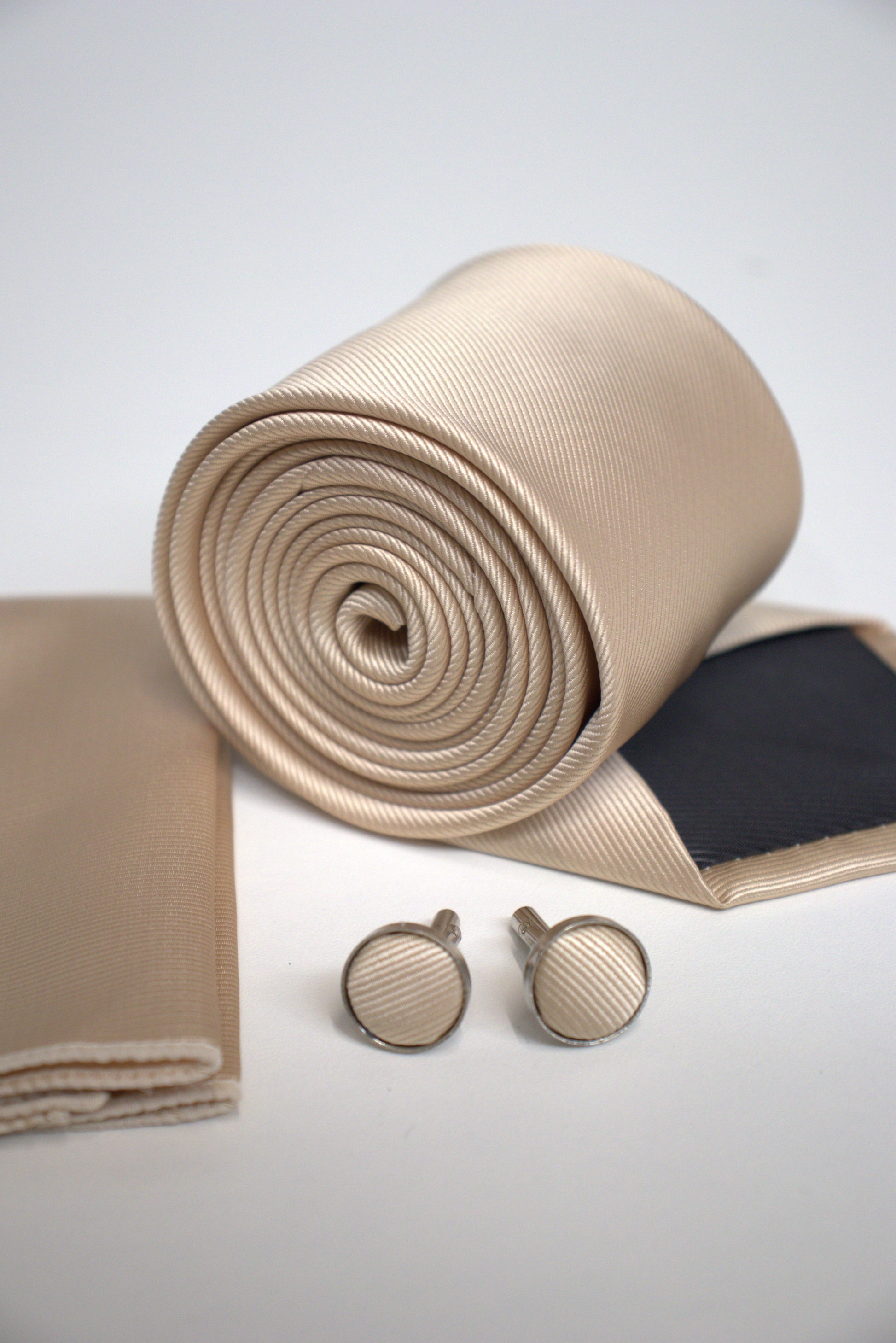 Close-up of champagne satin tie rolled with pocket square and cufflinks, elegant men’s accessory for weddings and formal events