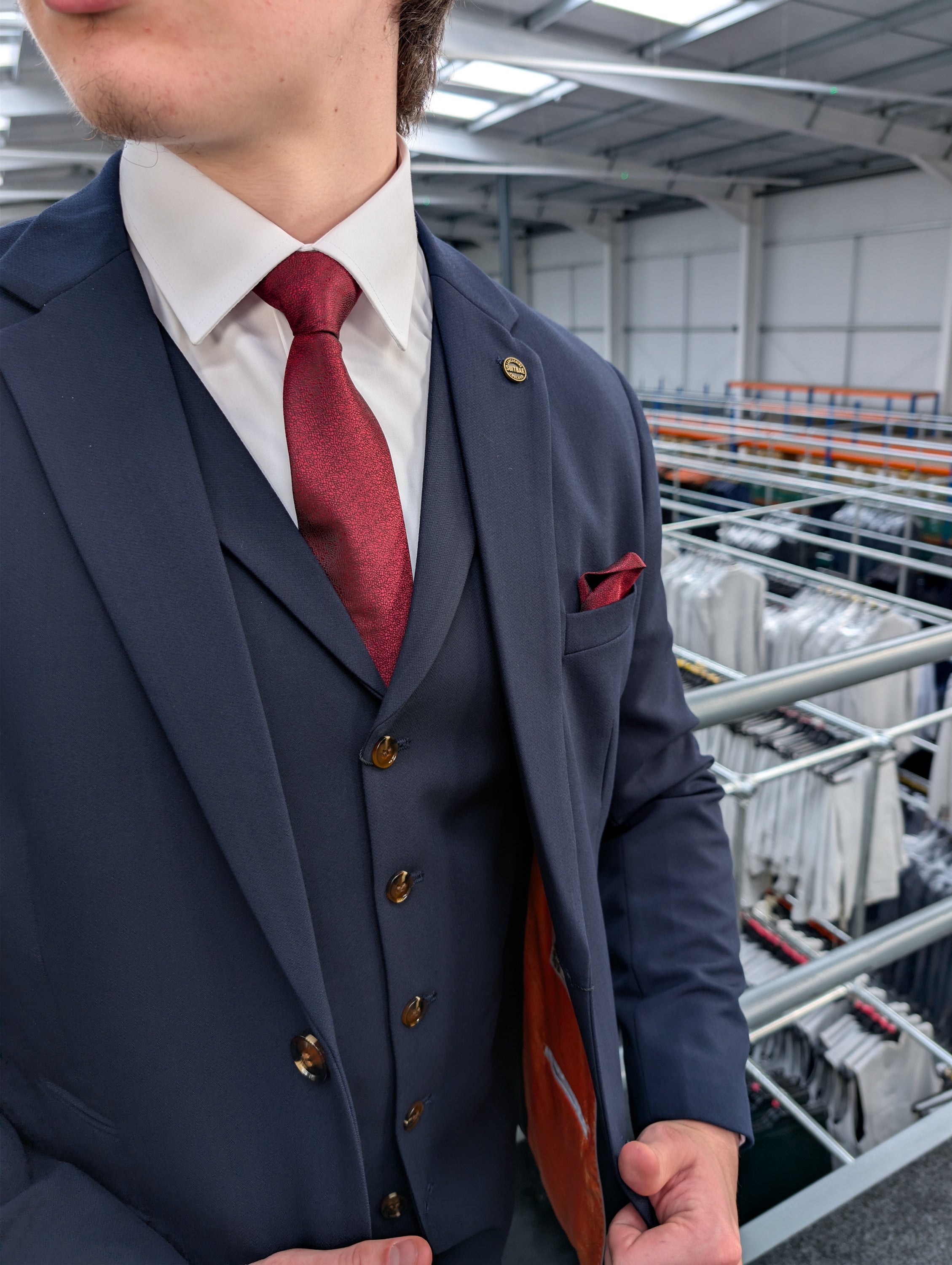 Close-up styling of a men's navy wedding suit accessorized with a textured burgundy tie, a pocket square, and a crisp white shirt.