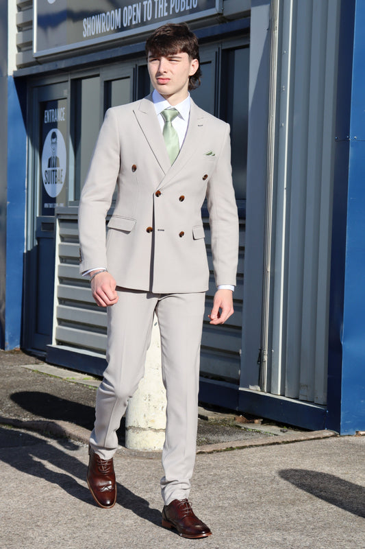 Model walking outside SUITBAE wearing the Escobar Stone Double-Breasted Suit with a sage green tie and brown brogues, showcasing a modern tailored fit ideal for weddings, proms, and race day events.