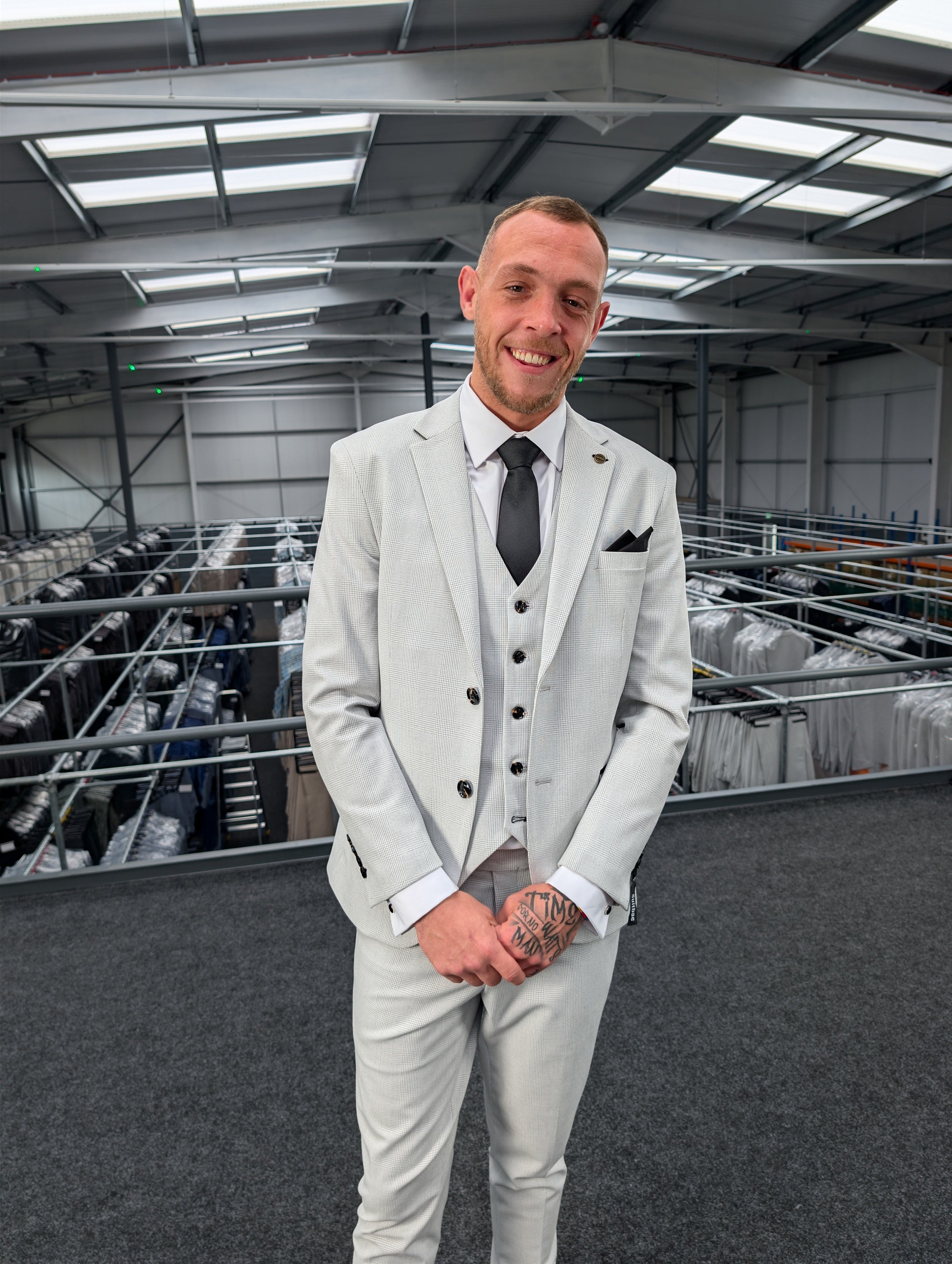 A men's light grey wedding suit in a fine checkered print, featuring a matching waistcoat, crisp white shirt, dark tie, and pocket square.