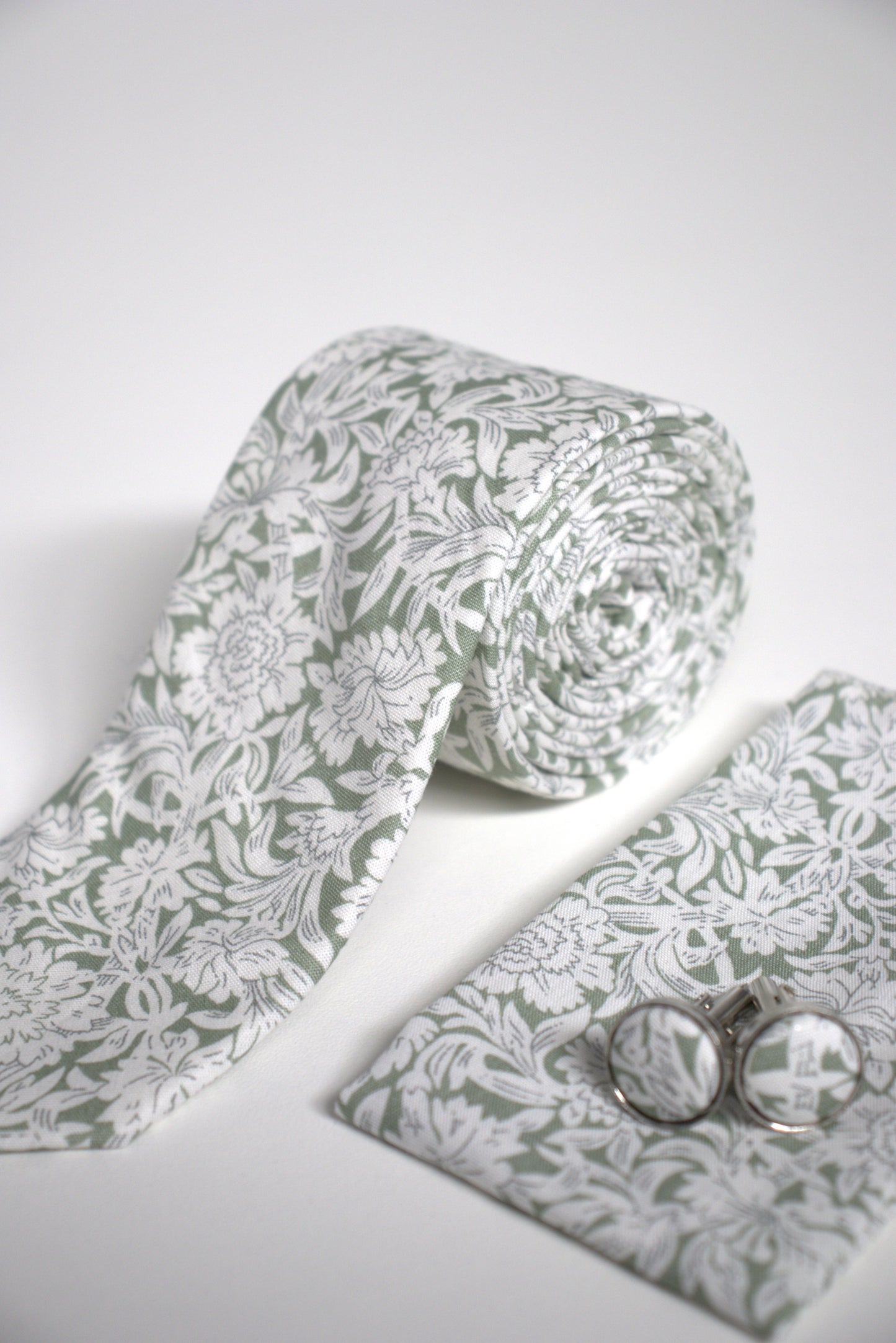 Close-up of sage green floral tie with pocket square and cufflinks, stylish groomsmen accessory for weddings, proms and formal occasions