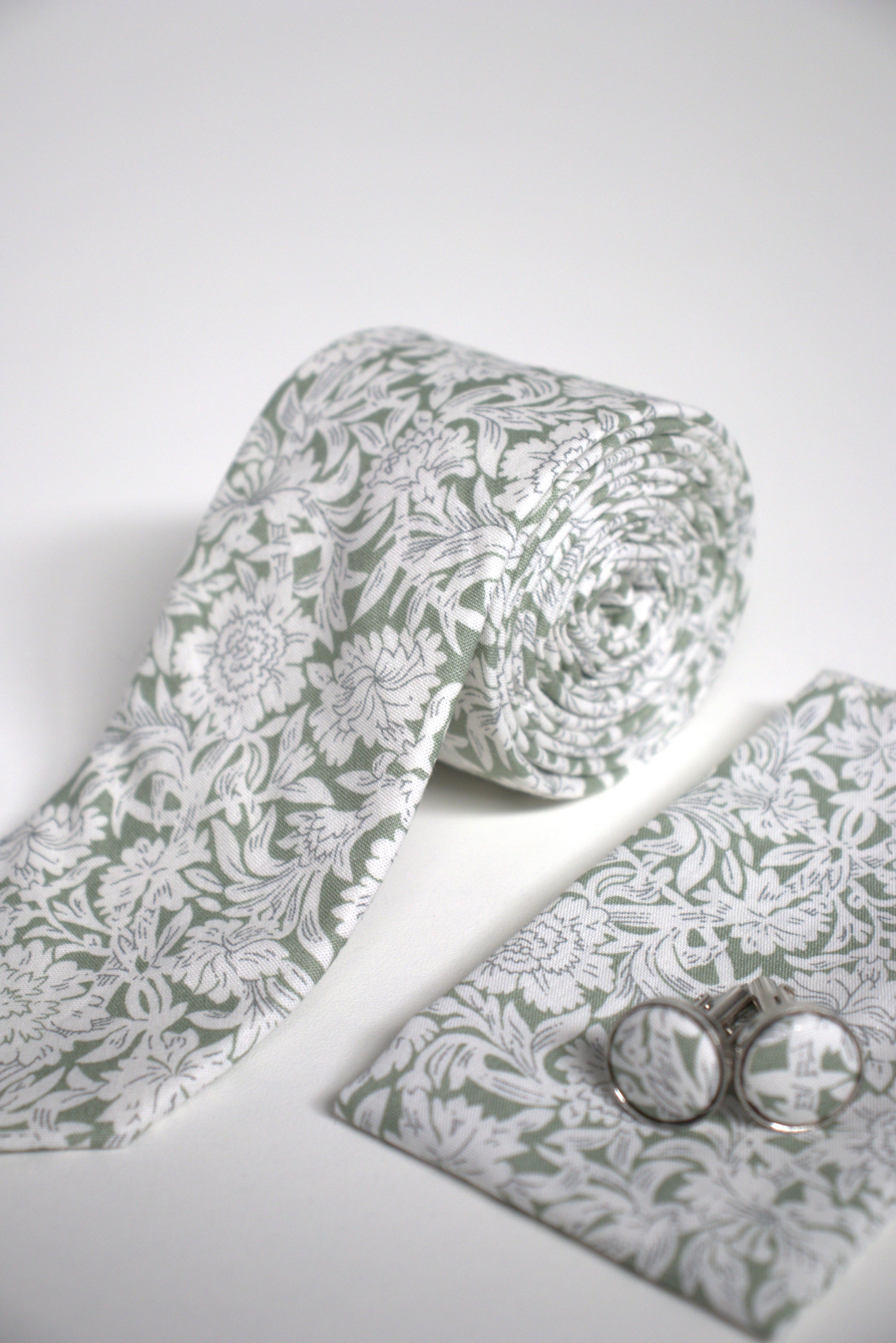 Close-up of sage green floral tie with pocket square and cufflinks, stylish groomsmen accessory for weddings, proms and formal occasions