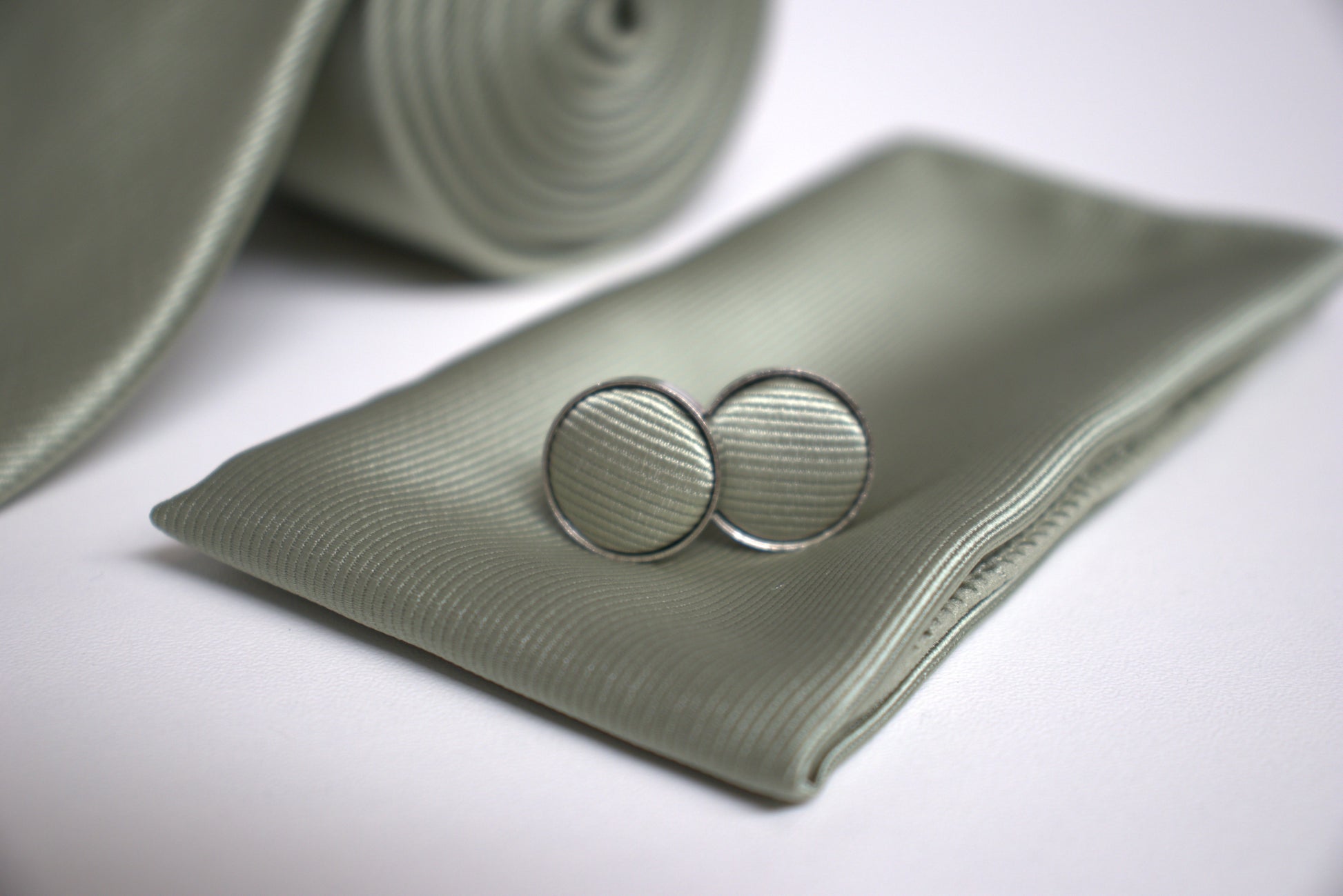 Close-up of sage green pocket square and cufflinks, elegant groomsmen accessories for prom, races and special occasions.