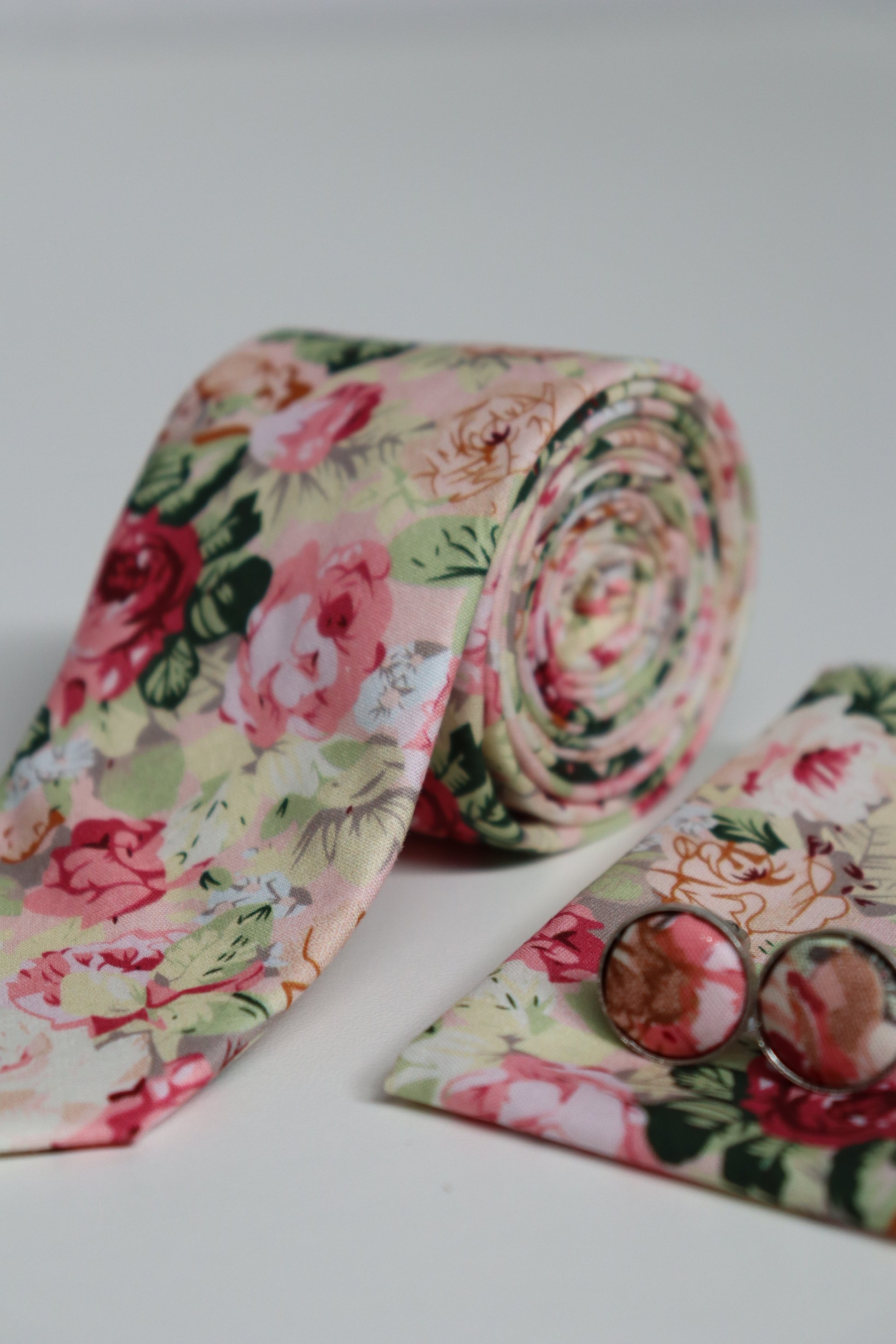 Close-up of vintage floral pink tie with matching pocket square and cufflinks, stylish accessory set for groomsmen